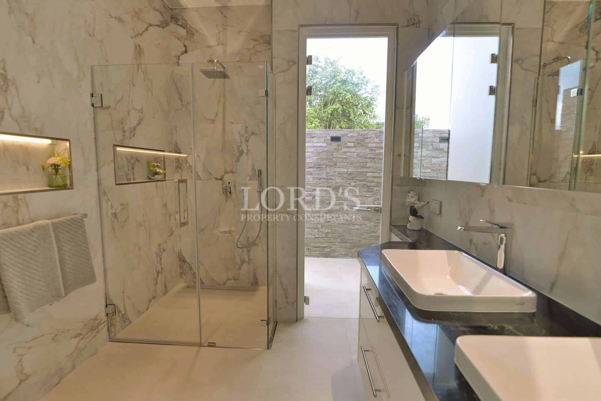 Modern marble bathroom with glass shower enclosure, double vanity, and natural light.
