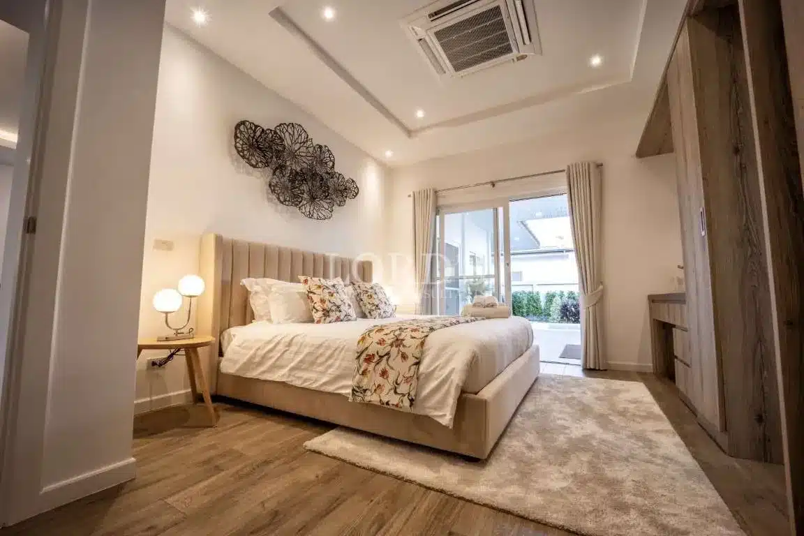 Luxury modern bedroom with upholstered king bed, decorative wall art, wooden flooring, and glass doors opening to a private outdoor area.