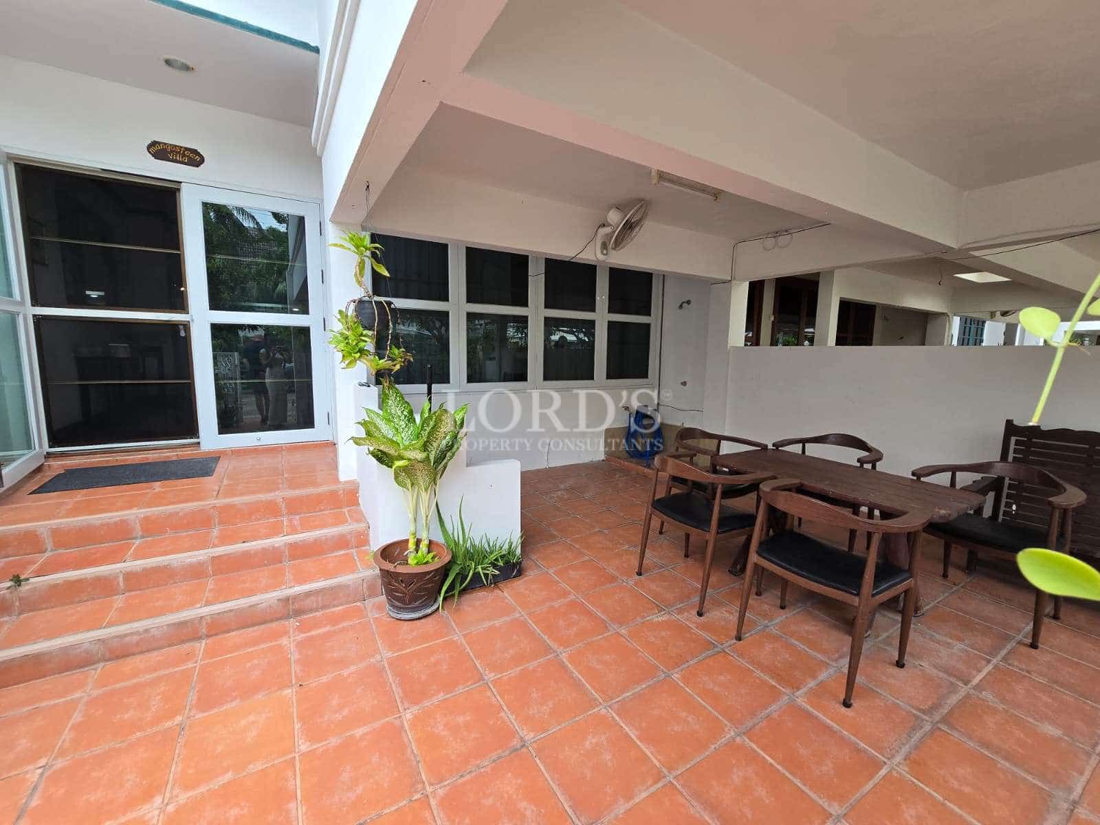 Covered outdoor patio with terracotta tiles, wooden dining set, and glass entrance doors.
