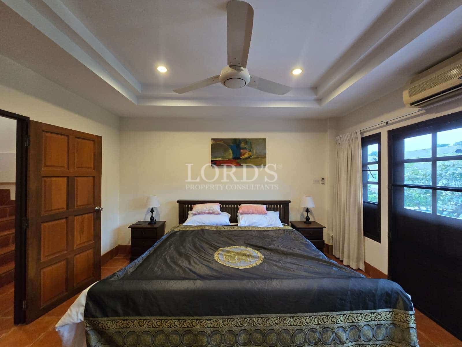 Spacious bedroom with double bed, ceiling fan, air conditioning, and wooden furniture.