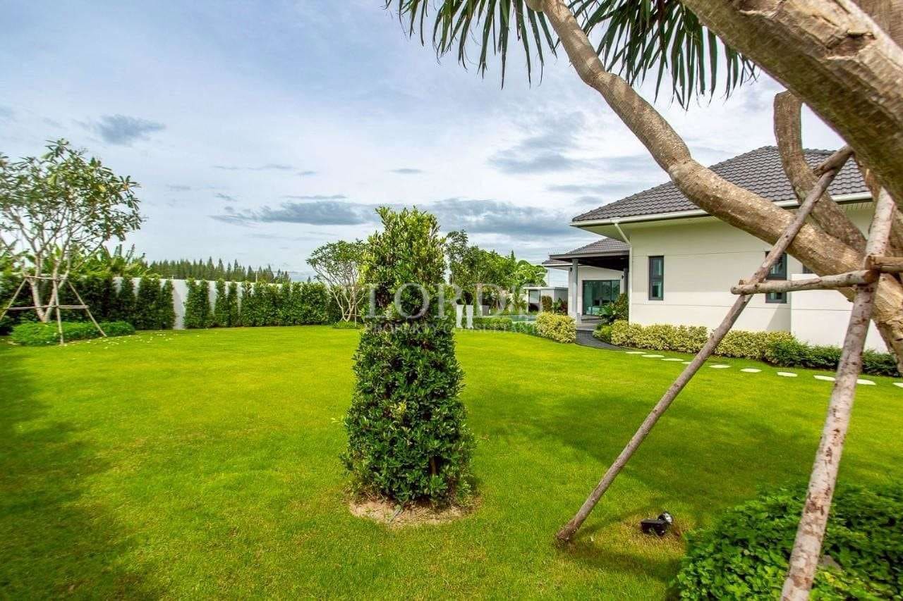 Spacious villa garden with manicured green lawn, tropical trees, and landscaped hedges.
