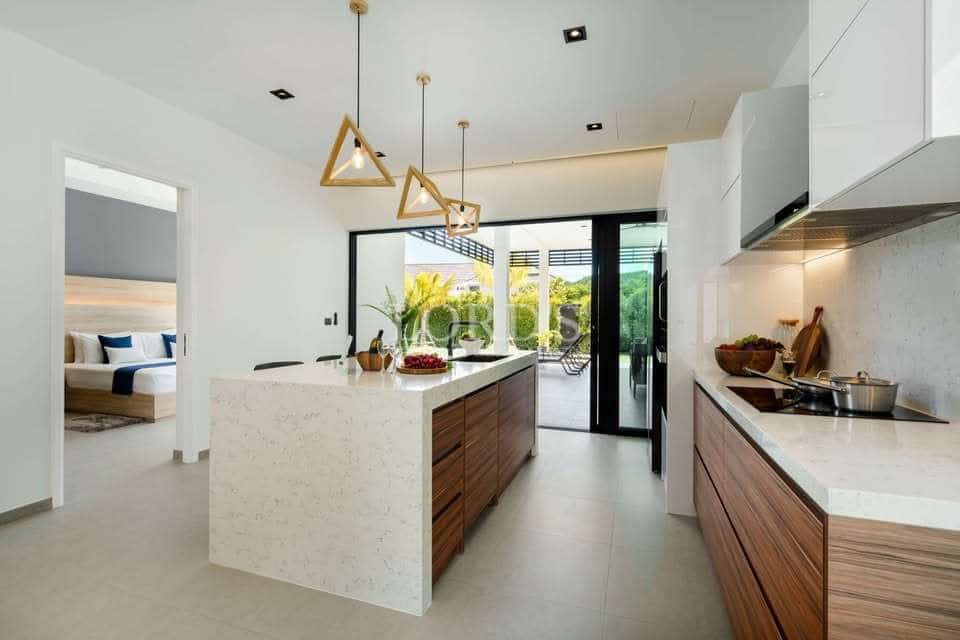 Modern open kitchen with white countertops, wooden cabinetry, island workspace, and geometric pendant lighting.
