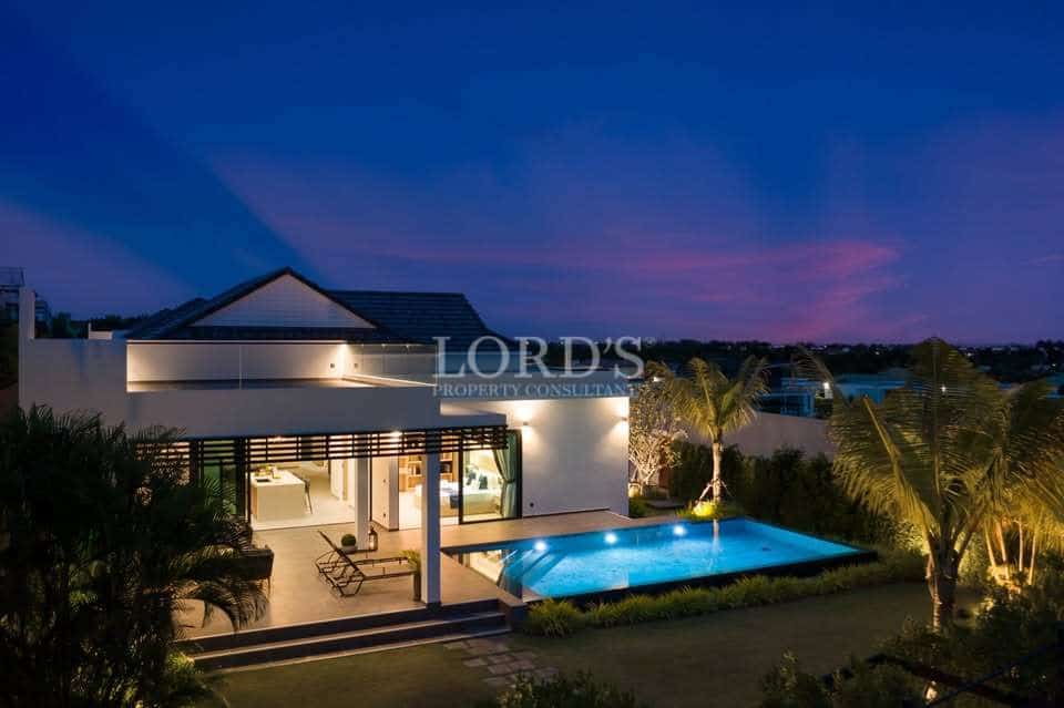 Luxury modern villa at night with illuminated private swimming pool, outdoor seating area, and landscaped garden.