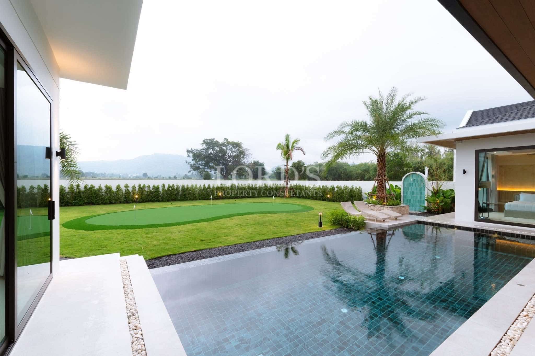 Luxury villa outdoor area with private swimming pool, landscaped garden, palm trees, and a putting green with mountain views.