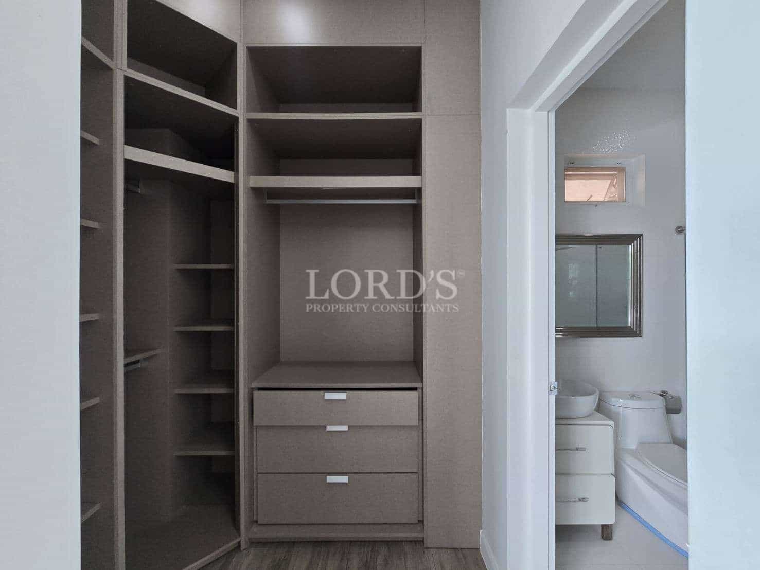 Built-in walk-in wardrobe with open shelving, hanging space, and drawers next to a modern bathroom.