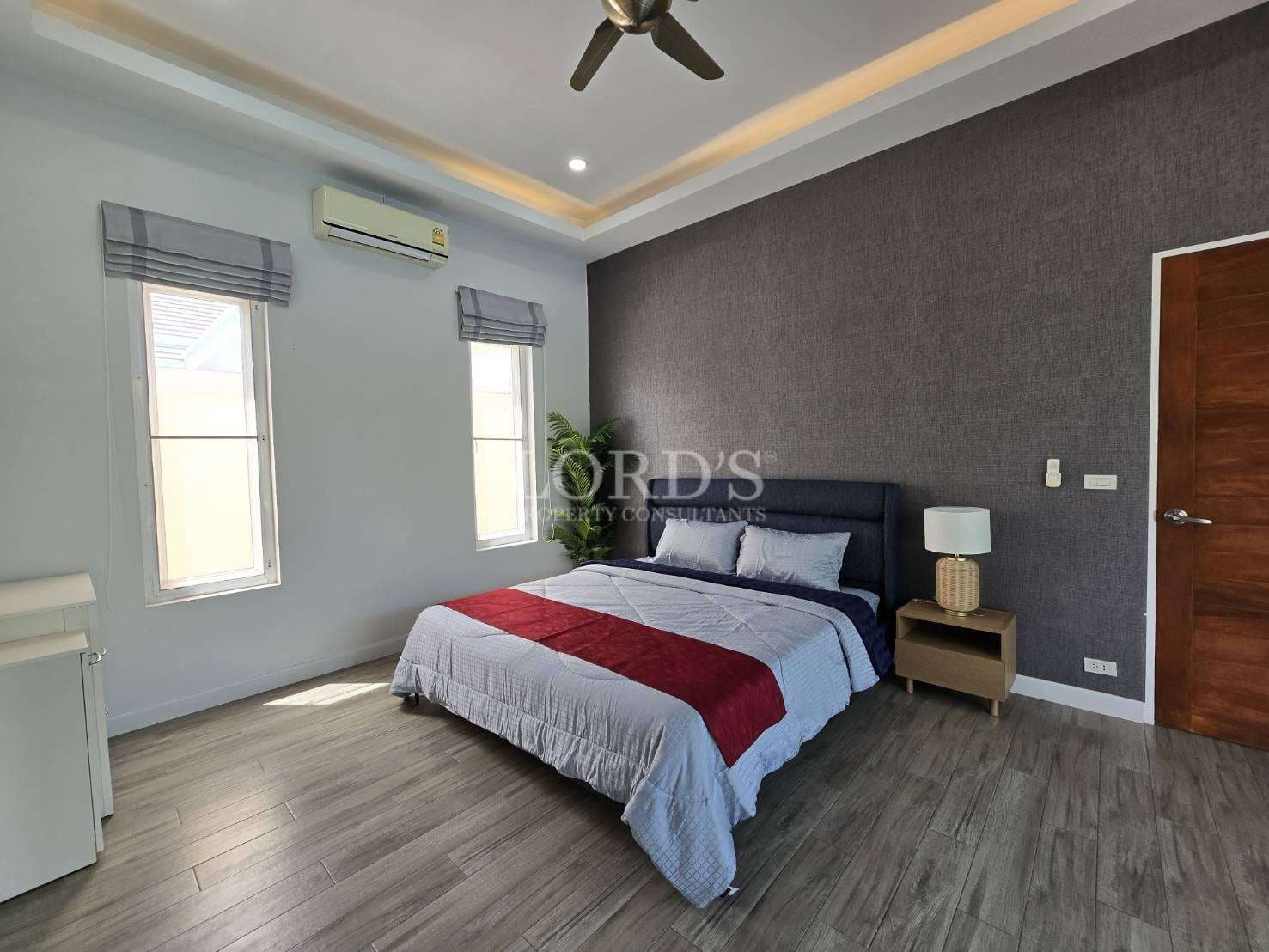 Modern bedroom with queen-size bed, accent wall, wooden flooring, and soft ambient ceiling lighting.