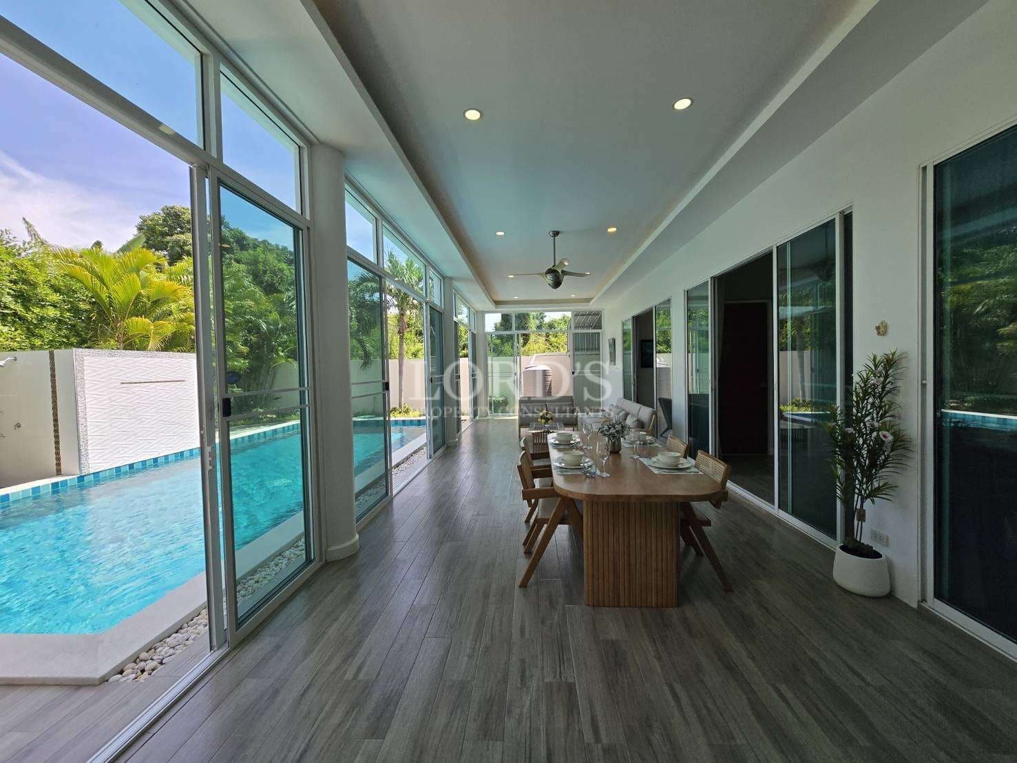 Covered outdoor dining area beside a private swimming pool with floor-to-ceiling glass walls.