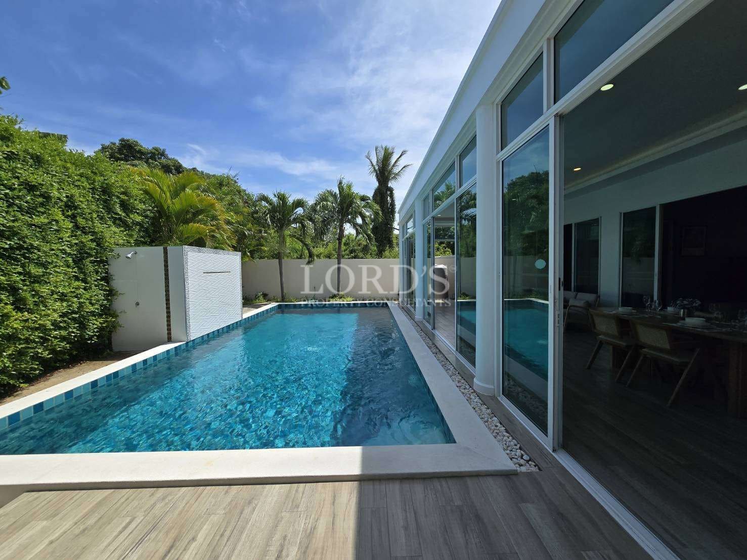 Private swimming pool beside a modern villa with floor-to-ceiling glass windows.