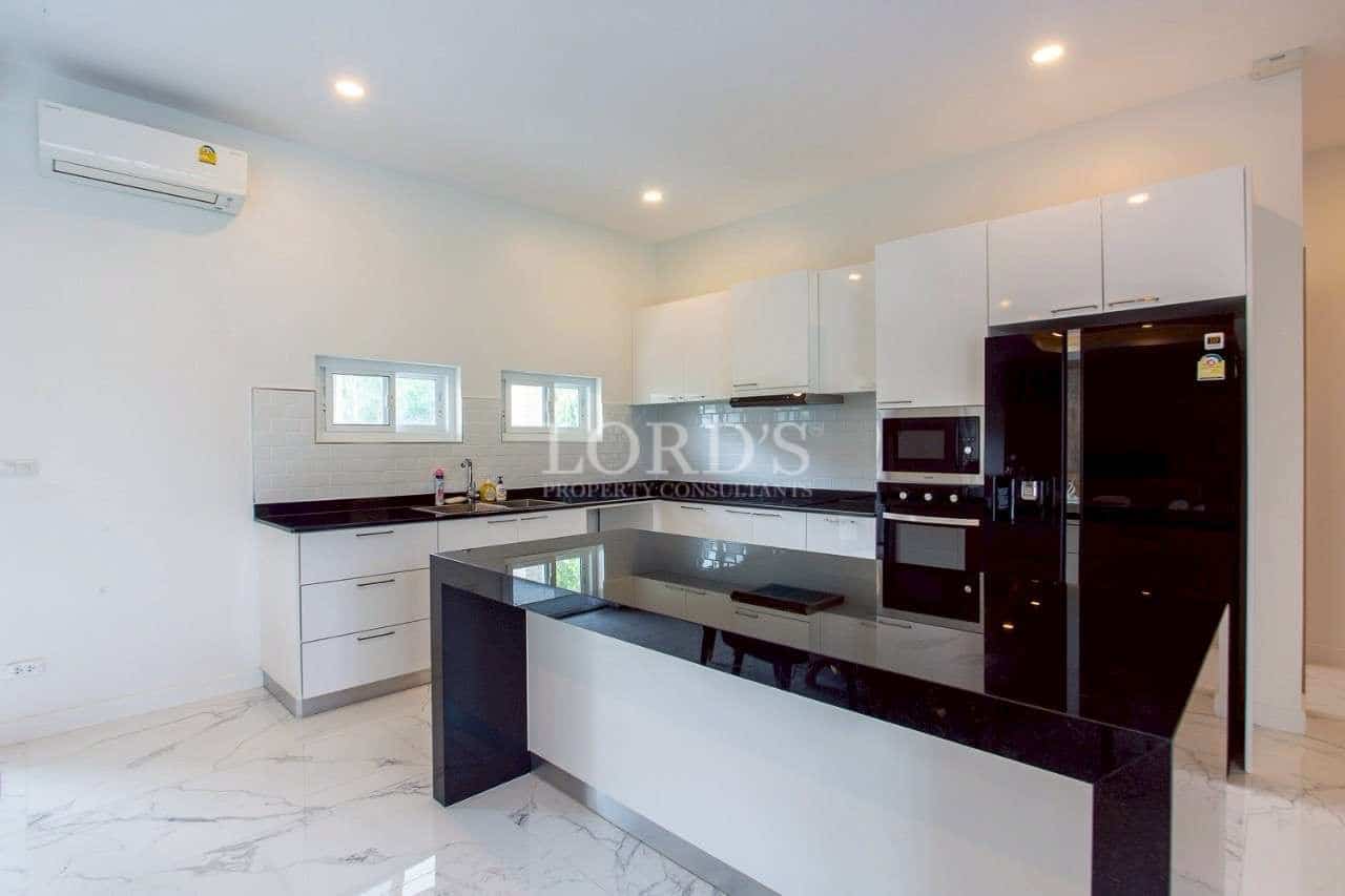 Modern white kitchen with black stone island, built-in appliances, and minimalist cabinetry.