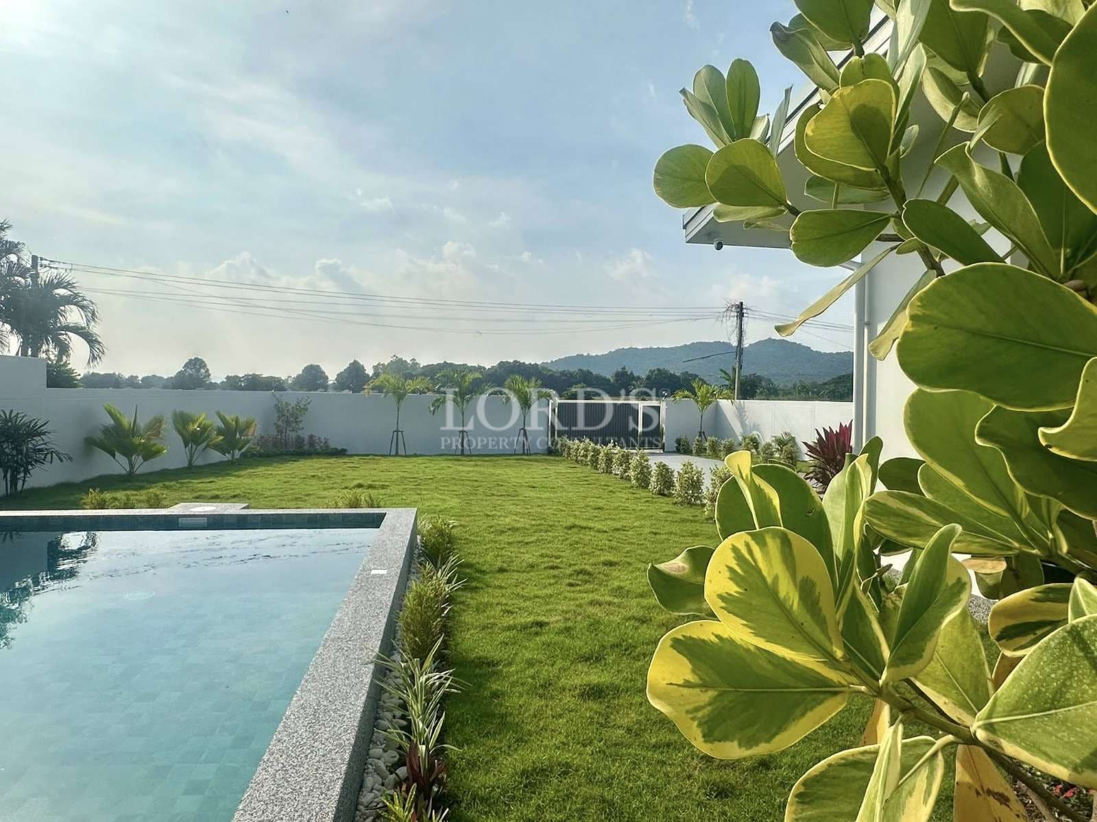 Private garden with manicured green lawn, swimming pool edge, tropical plants, and scenic mountain views.