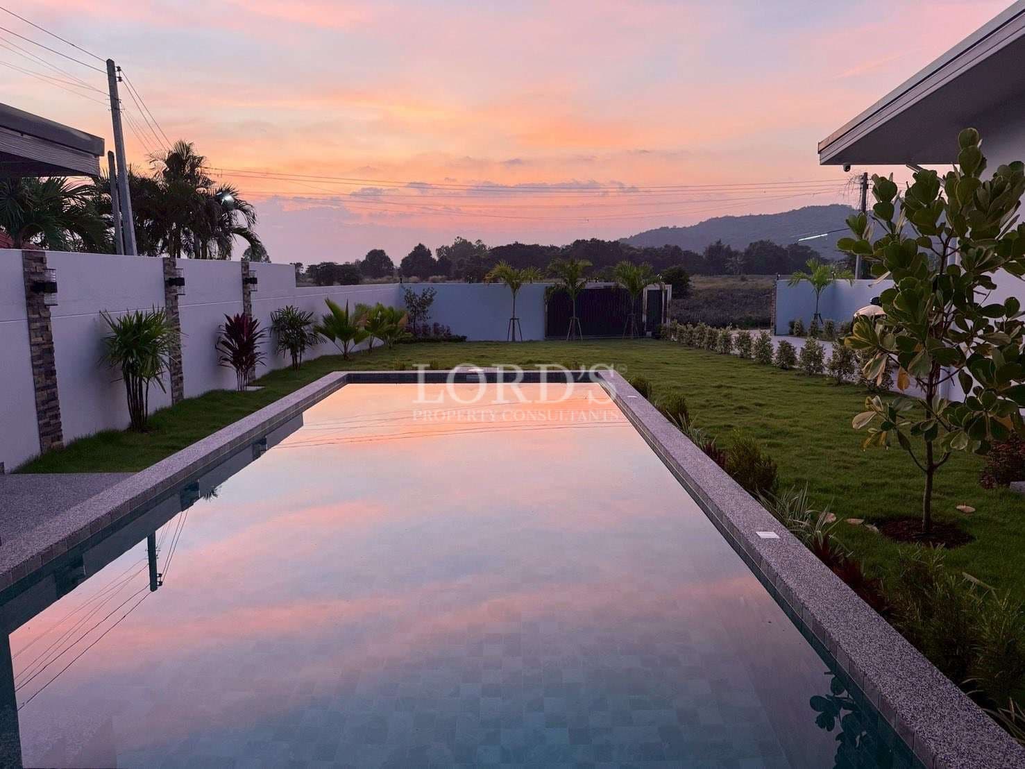 Infinity swimming pool reflecting sunset sky with landscaped garden and mountain views