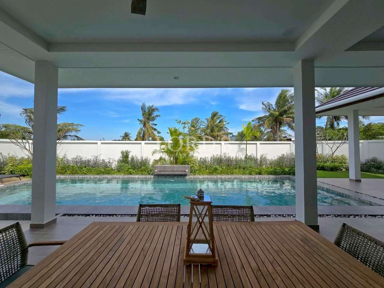 Covered outdoor dining area overlooking a private swimming pool and tropical garden.