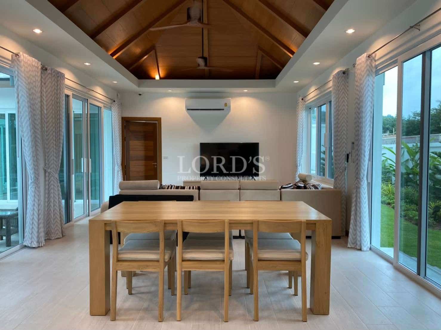 Spacious open-plan living and dining area with wooden dining table, vaulted ceiling, large glass doors, and modern furnishings.