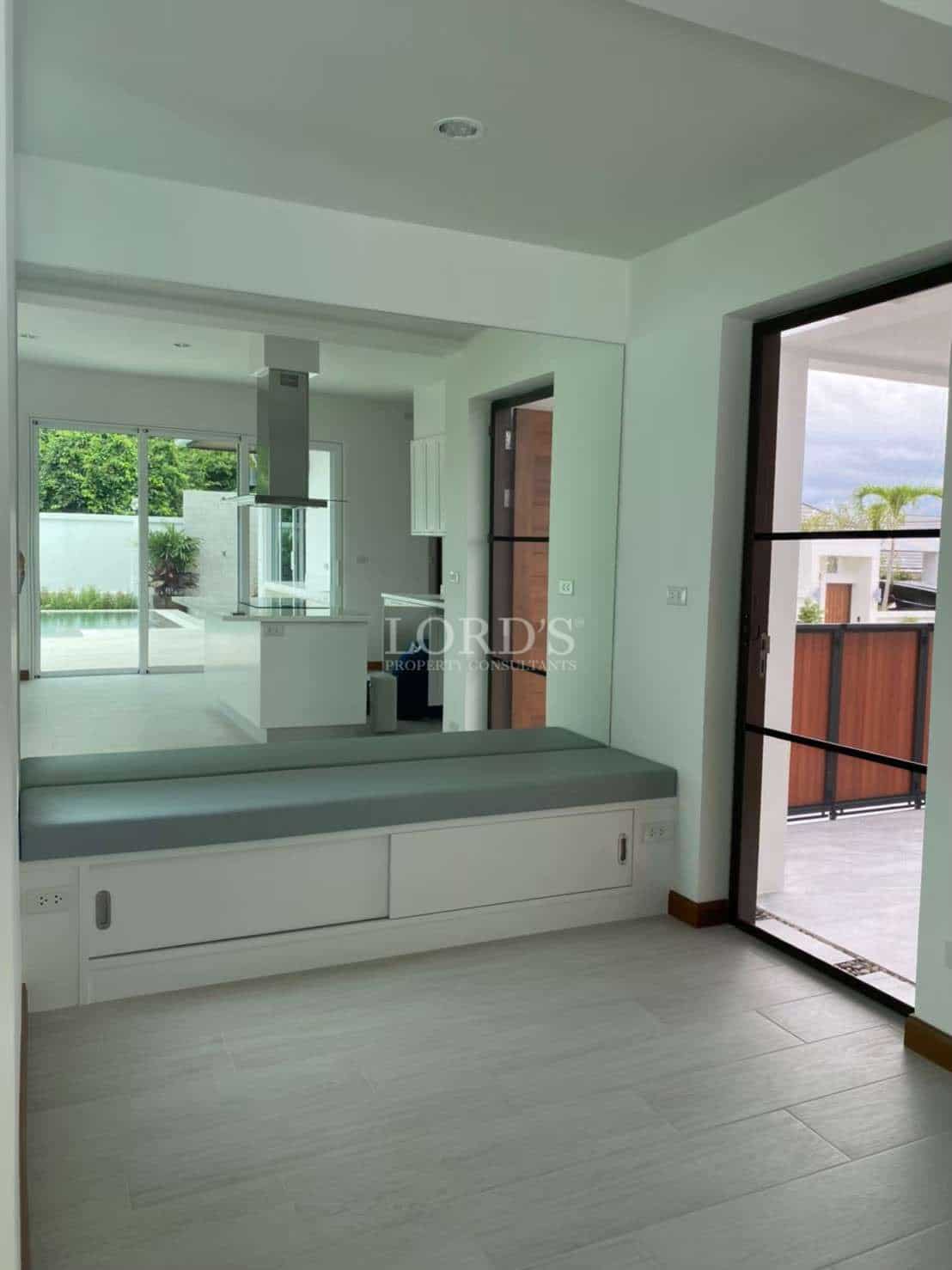 Minimalist interior hallway with built-in bench seating, large wall mirror, and glass door leading outdoors.