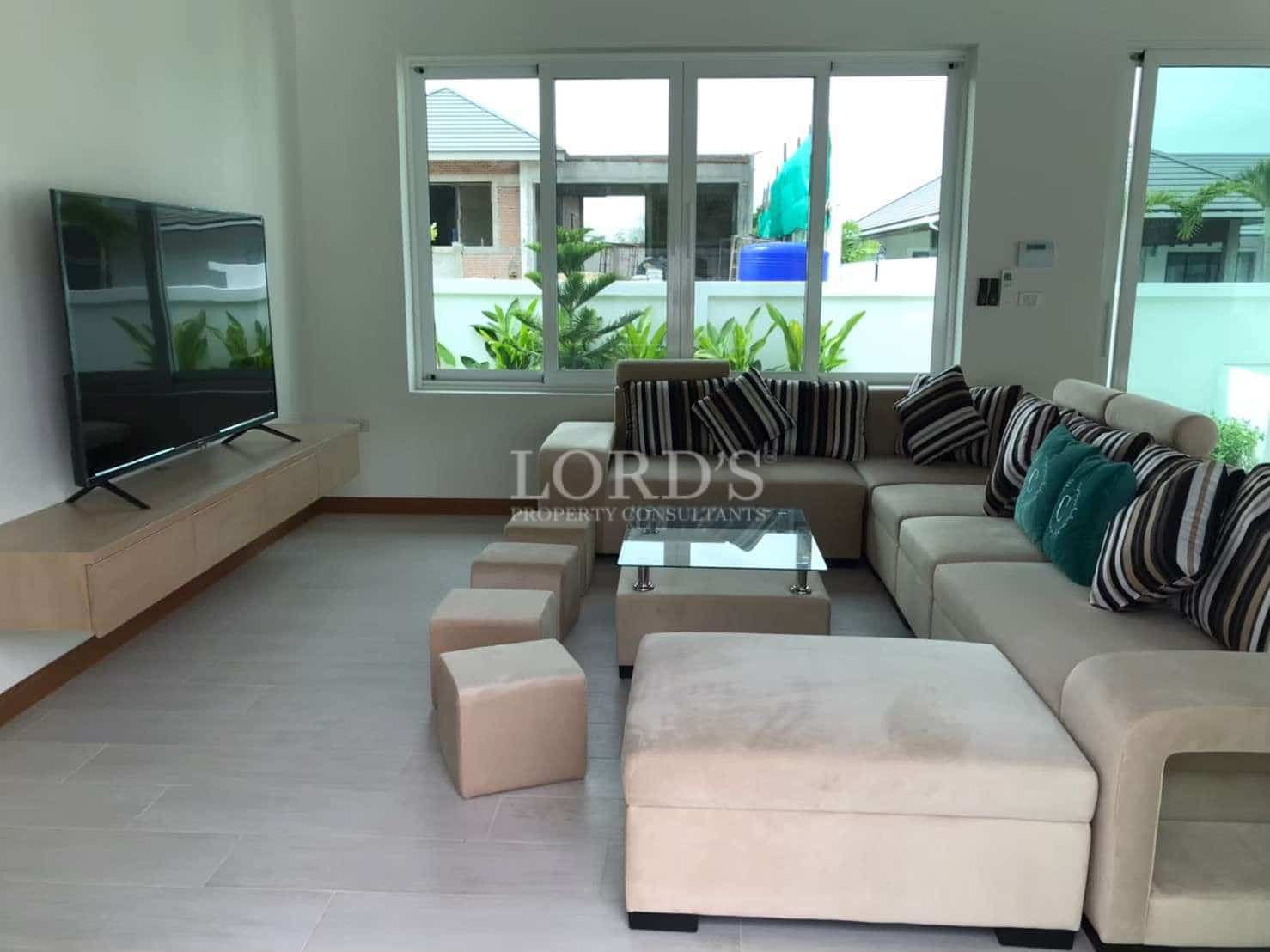 Modern living room with sectional sofa, wall-mounted television, large windows, and neutral interior design.