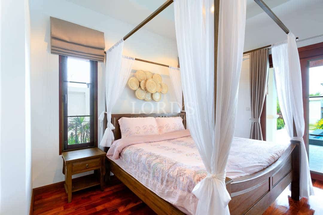 Luxury bedroom with a wooden four-poster bed, sheer white canopy curtains, soft pink bedding, and polished wooden floors.