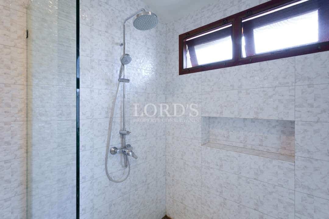 Modern walk-in shower with rainfall showerhead, glass partition, built-in wall niche, and natural light from a window.