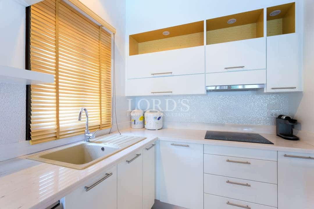 Modern white kitchen with built-in cabinets, stone countertop, stainless sink, and natural light from window blinds