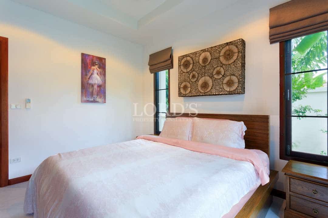Luxury villa bedroom with wooden bed, soft pink bedding, decorative wall art, and garden view window