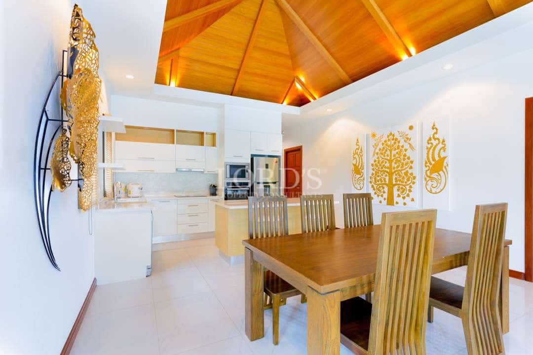 Luxury villa dining area with wooden table, modern white kitchen, and high vaulted wood ceiling