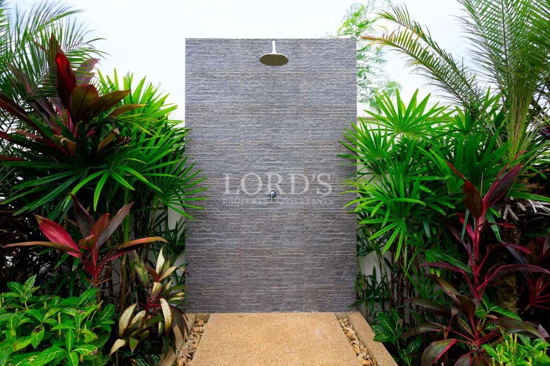 Outdoor rain shower in luxury villa garden surrounded by tropical plants and stone feature wall
