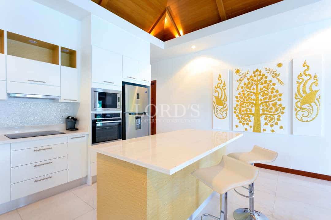 Luxury white kitchen with large island, built-in oven, stainless steel fridge, and gold wall art