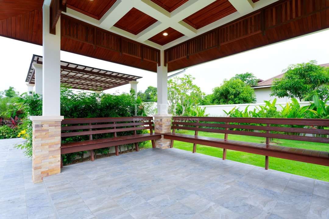 Covered outdoor pavilion with wooden seating and landscaped garden in luxury villa