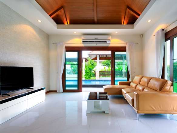 Modern living room with leather sofa, wood ceiling, and sliding doors opening to private pool