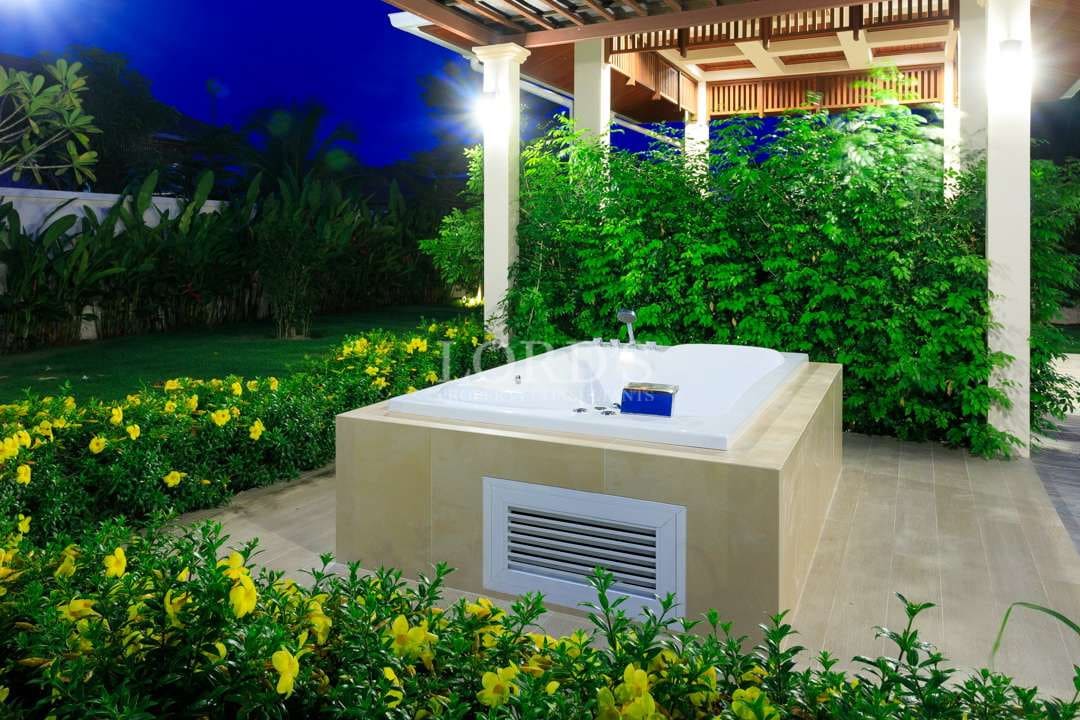 Outdoor jacuzzi under pergola surrounded by tropical garden with soft nighttime lighting