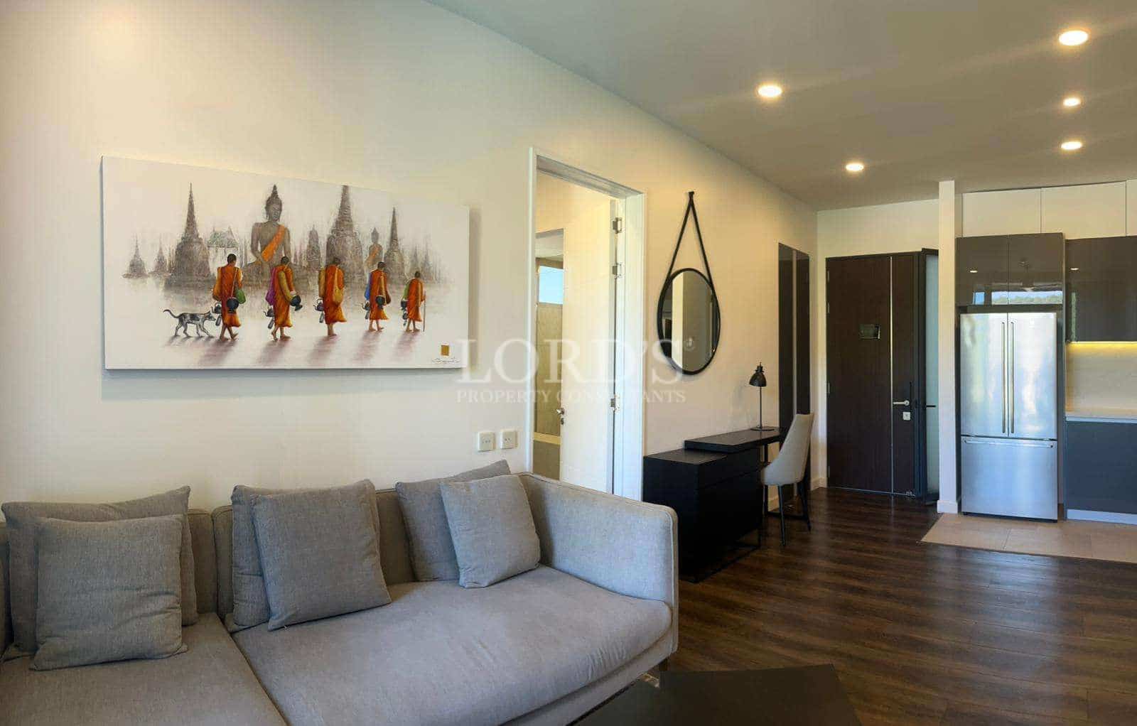 Modern living room with sofa, wall art, work desk, and open-plan kitchen in the background