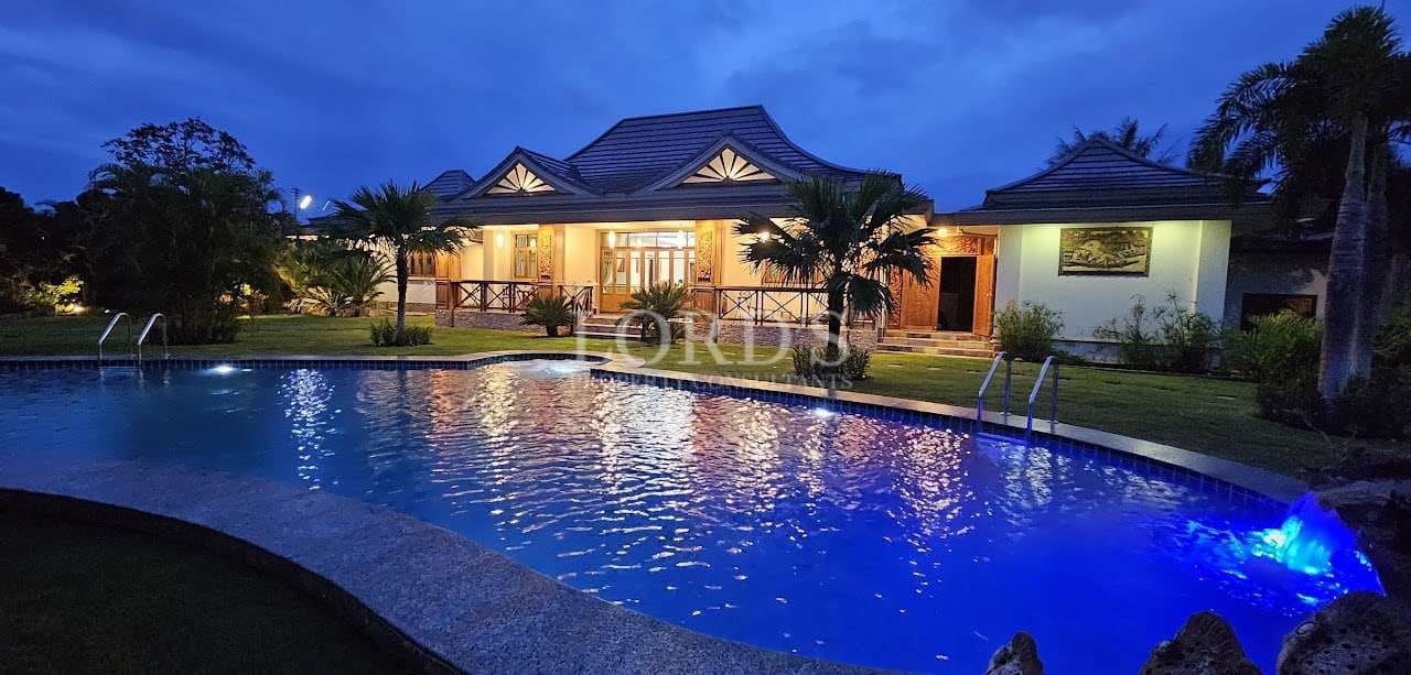 Luxury villa with private swimming pool at night, tropical garden, warm exterior lighting, and modern pavilion-style architecture