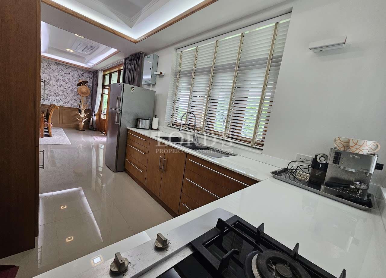 Modern open kitchen with white countertops, wooden cabinets, gas cooktop, stainless steel refrigerator, and large windows with blinds