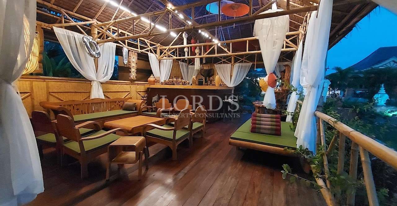 Open-air bamboo pavilion with wooden seating, soft draped curtains, and ambient lighting overlooking a tropical garden at dusk.