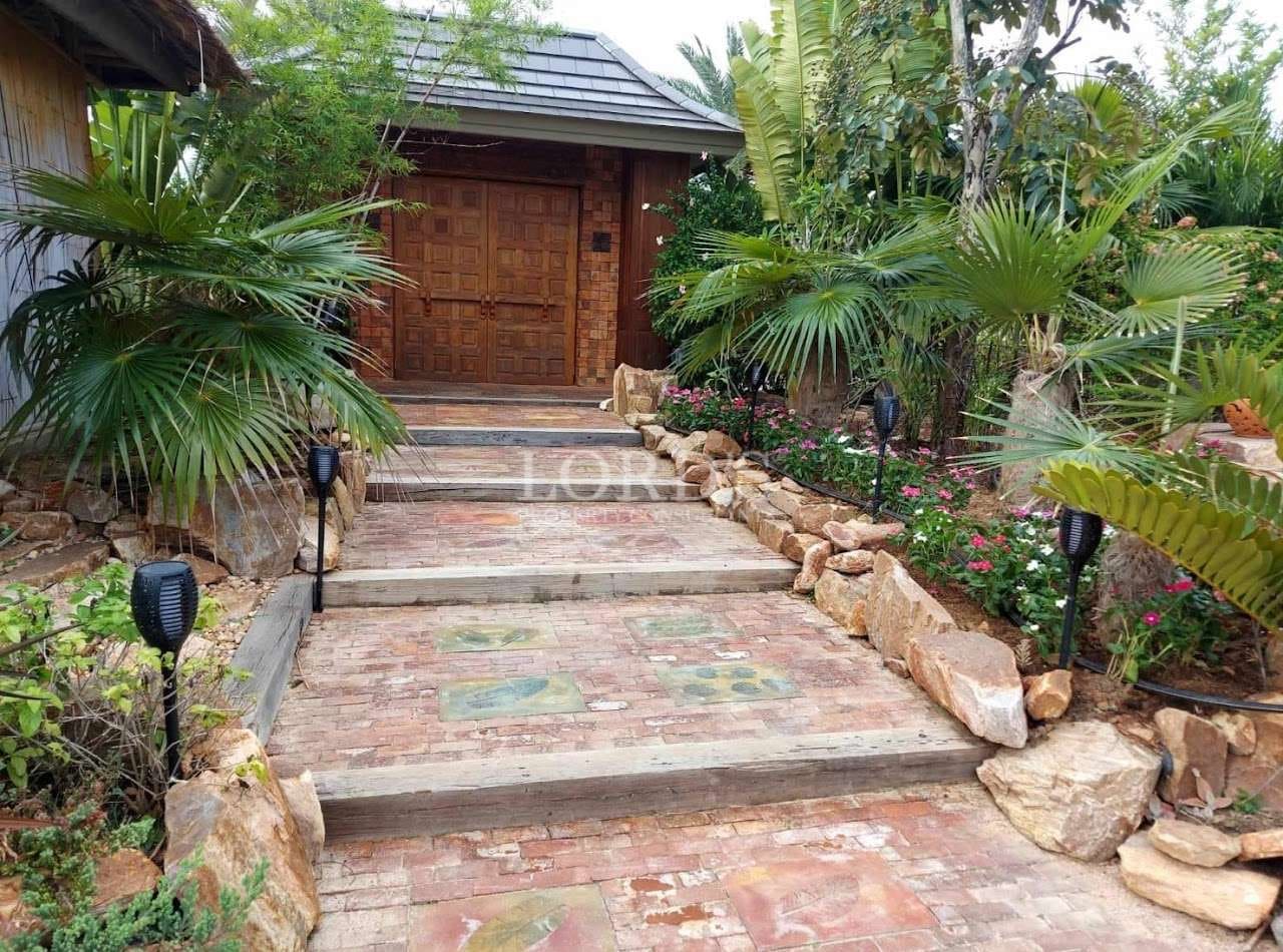 Stone-paved garden walkway leading to a traditional wooden entrance surrounded by lush tropical landscaping.