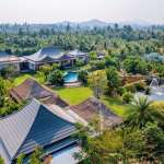 Aerial view of a luxury villa estate surrounded by palm trees, landscaped gardens, swimming pool, and natural pond.