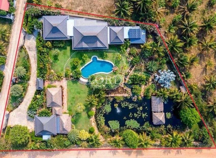 Top-down aerial view of a private estate with villas, swimming pool, pond, landscaped gardens, and marked land boundaries.