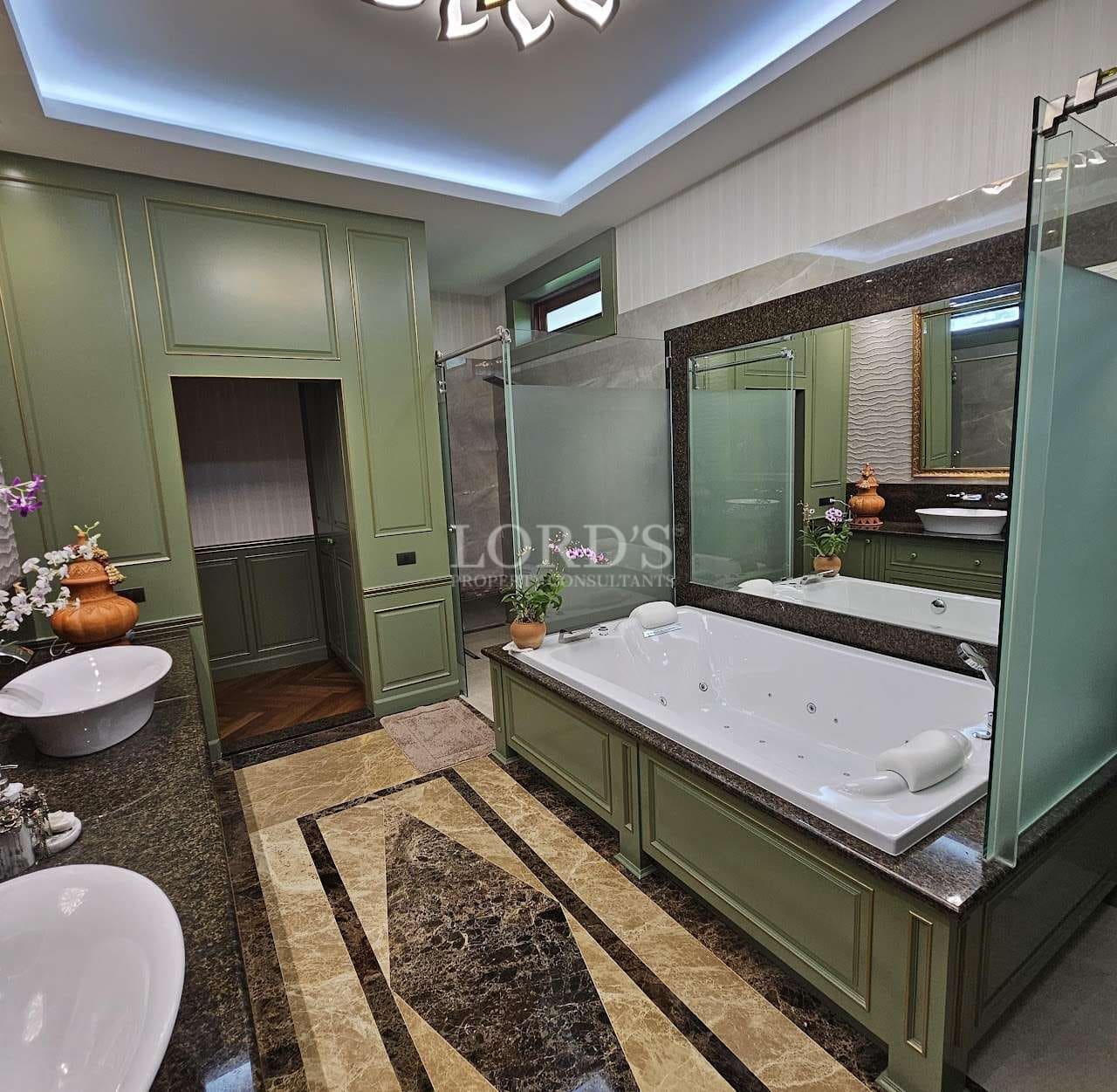 Luxury bathroom with built-in jacuzzi bathtub, green cabinetry, glass shower enclosure, stone flooring, and ambient ceiling lighting