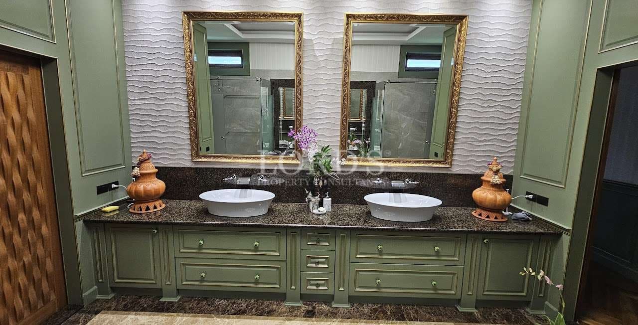 Luxury double vanity bathroom with green cabinetry, stone countertop, vessel sinks, textured wall tiles, and gold-framed mirrors