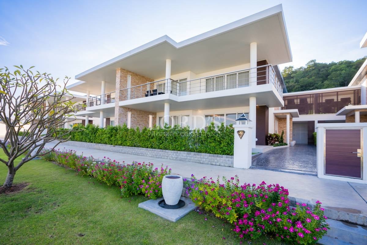 Modern two-story villa with balconies, landscaped garden, private driveway, and contemporary architecture.