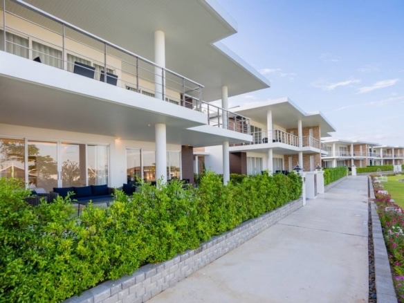 Modern residential villas with covered terraces, balconies, landscaped hedges, and pedestrian walkway.