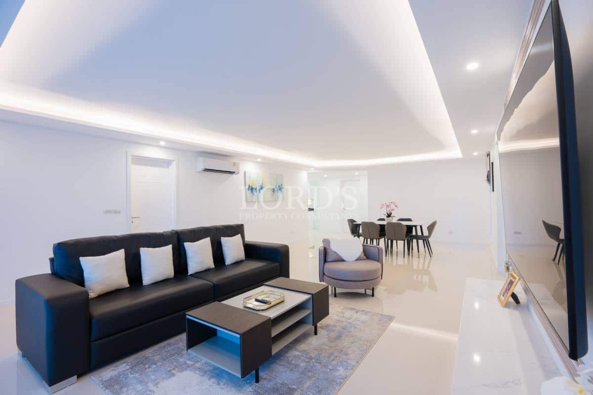 Modern open-plan living room with sectional sofa, feature TV wall, recessed ceiling lighting, and dining area.