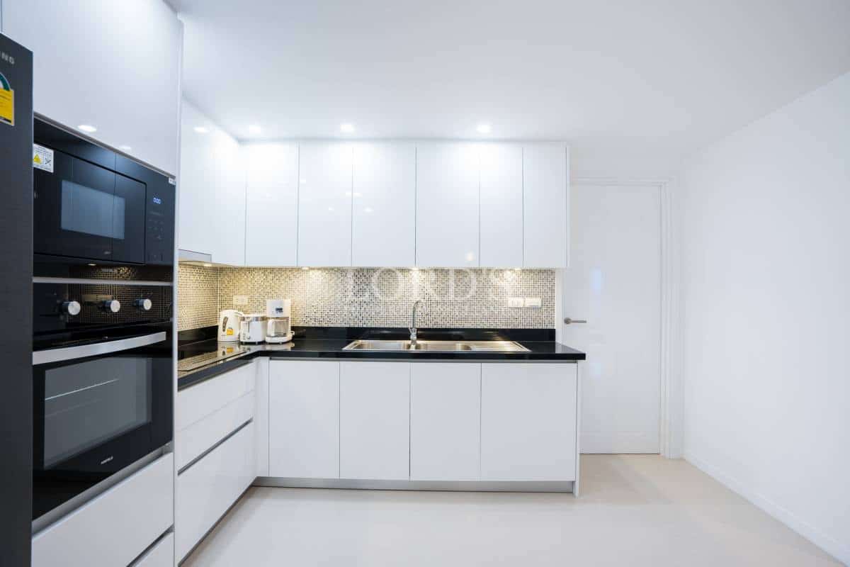 Minimalist white kitchen with built-in oven and microwave, black countertops, and mosaic tile backsplash.