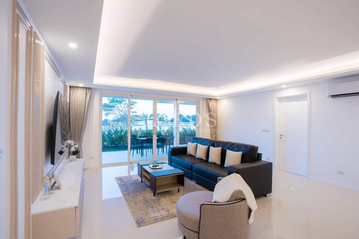 Modern living room with comfortable sofa, recessed ceiling lighting, wall-mounted TV, and sliding glass doors to the terrace.