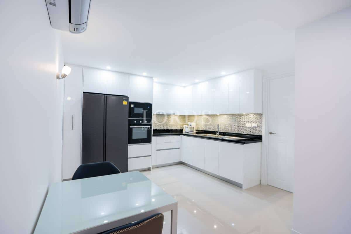 Bright modern kitchen with white cabinetry, black countertops, built-in appliances, and compact dining area.