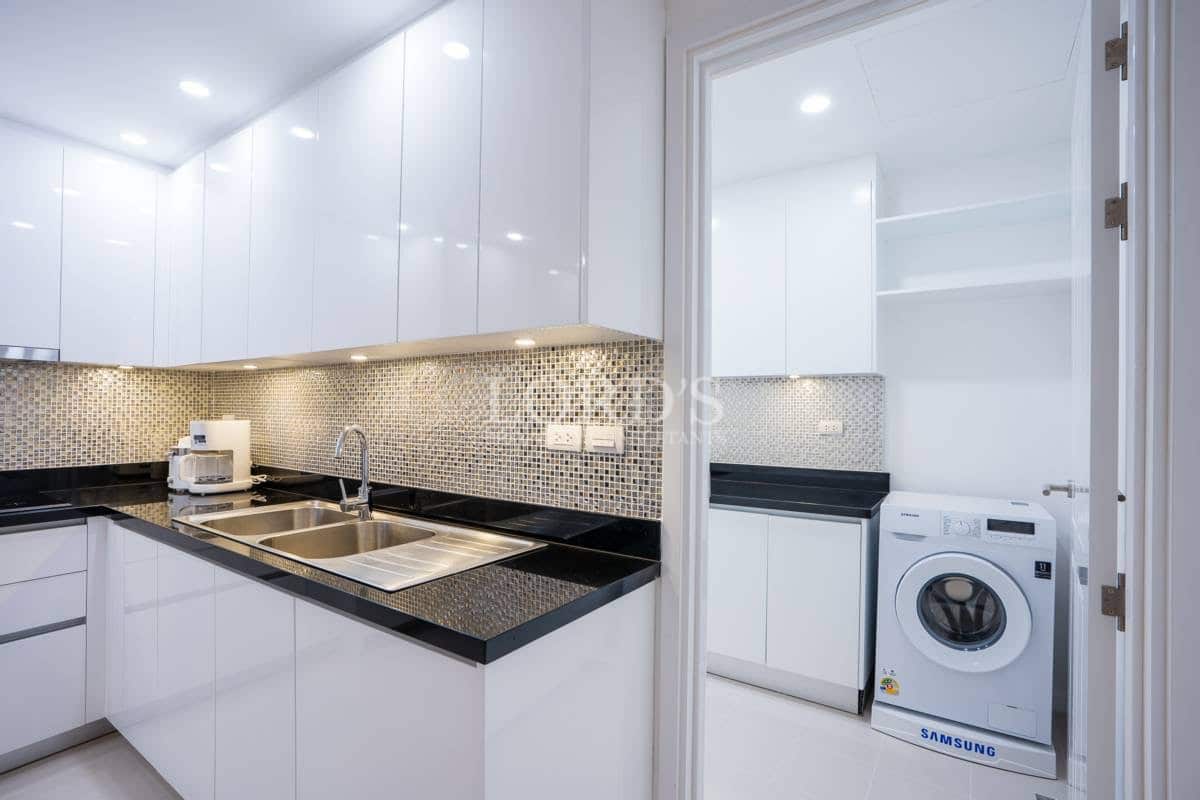 Modern kitchen with glossy white cabinets, black countertops, mosaic backsplash, and adjoining utility room with washing machine.