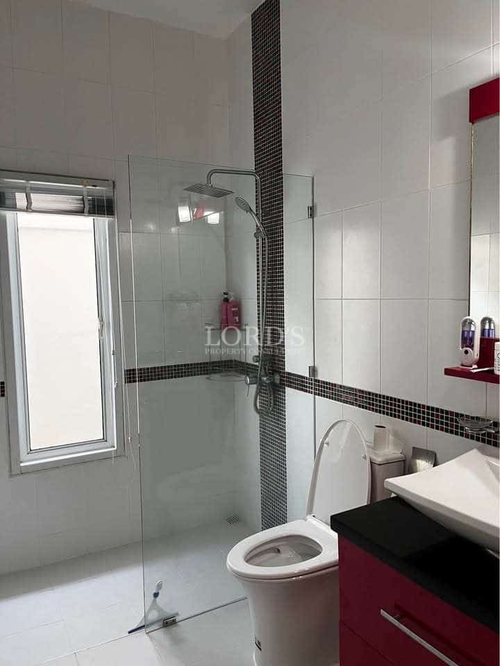 Modern bathroom with glass-enclosed shower, wall-mounted sink, toilet, white tiled walls, and window for natural light