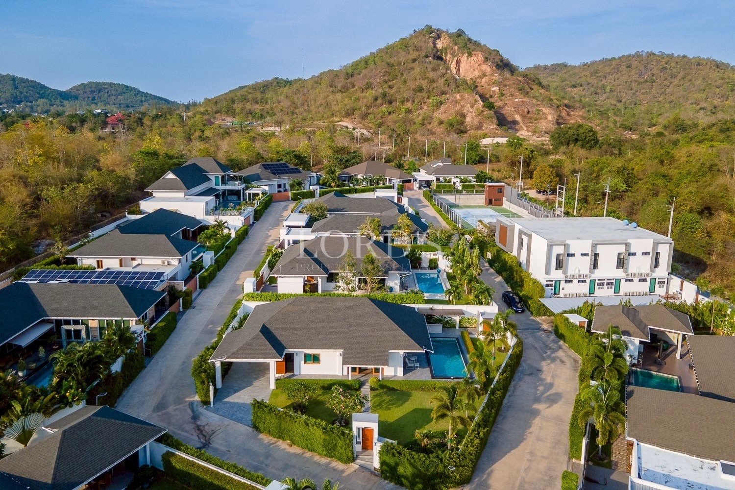 Aerial view of a luxury villa community with private pools, landscaped streets, and mountain backdrop.