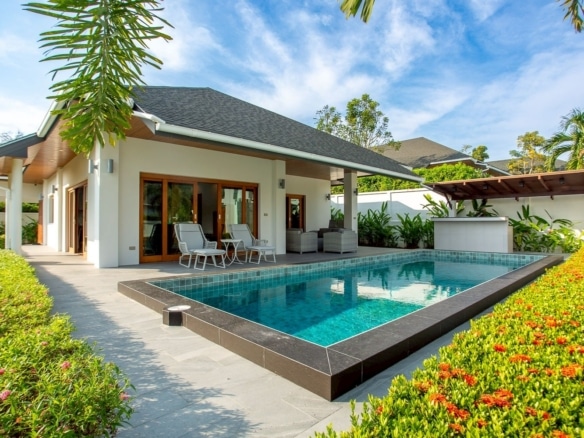 Luxury modern villa with a private swimming pool, outdoor seating area, and tropical garden under a bright blue sky.