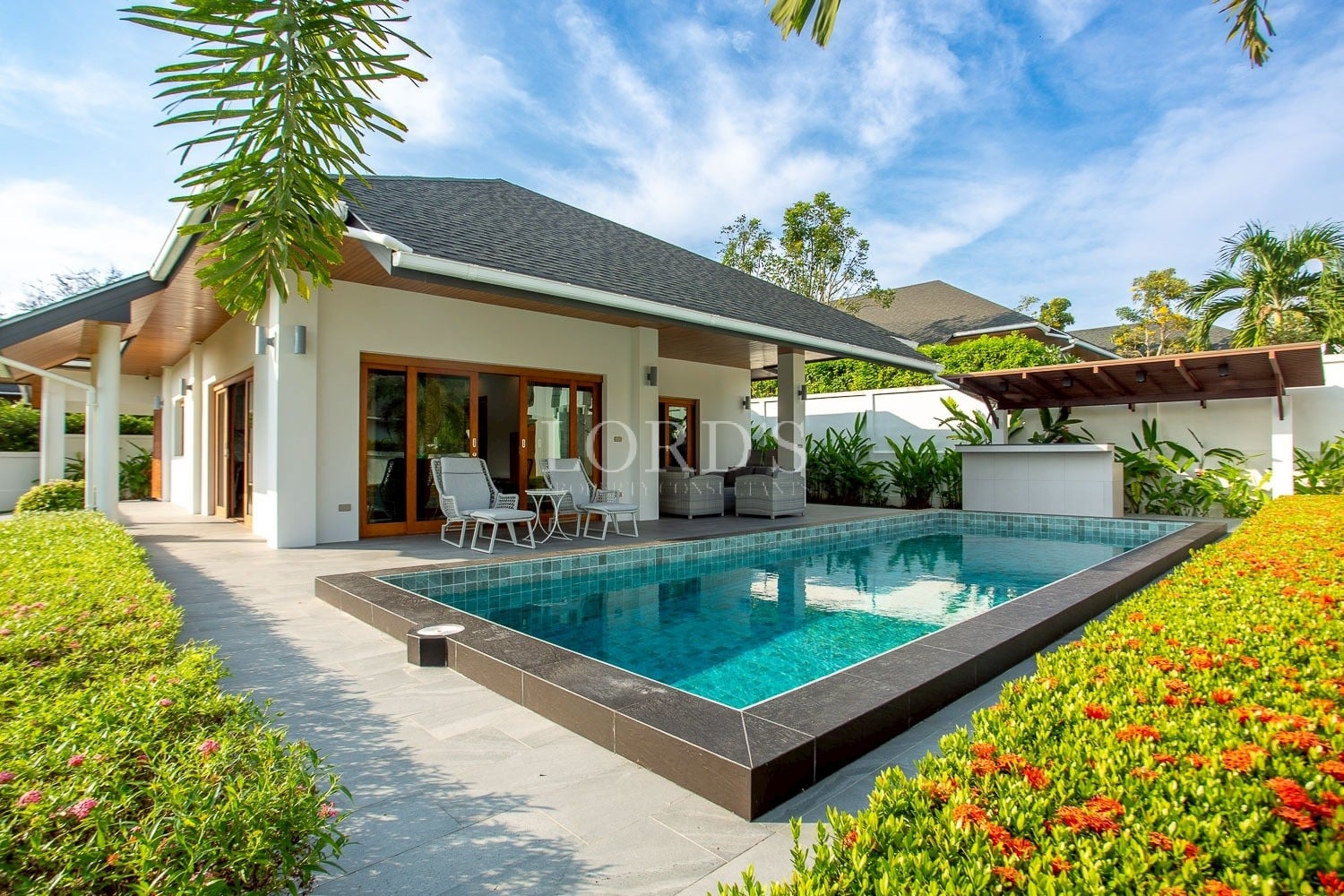 Luxury modern villa with a private swimming pool, outdoor seating area, and tropical garden under a bright blue sky.