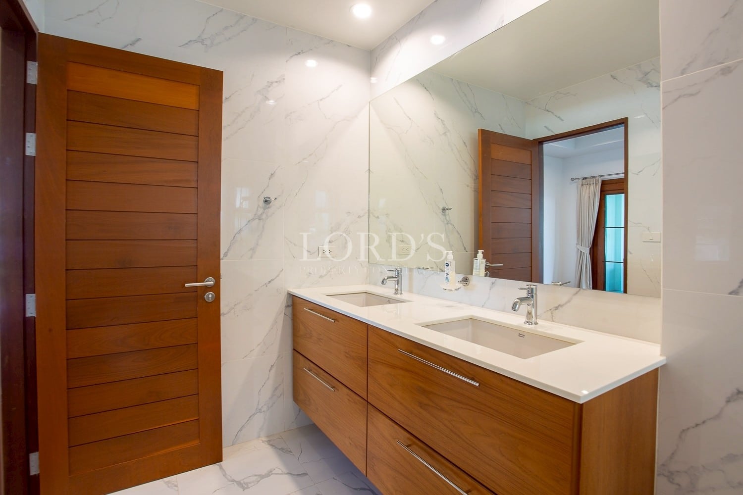 Modern bathroom with double sink vanity, marble walls, and wooden cabinetry